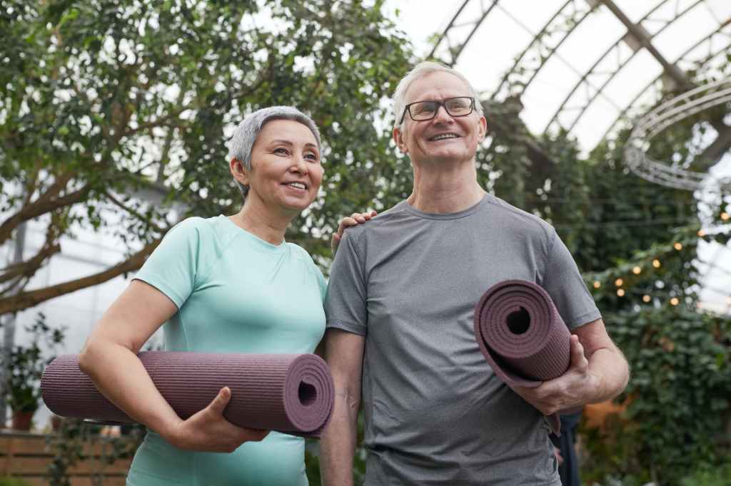 The image shows an older man and a woman, each carrying a yoga mat. 12 Powerful Benefits of Strength Training.