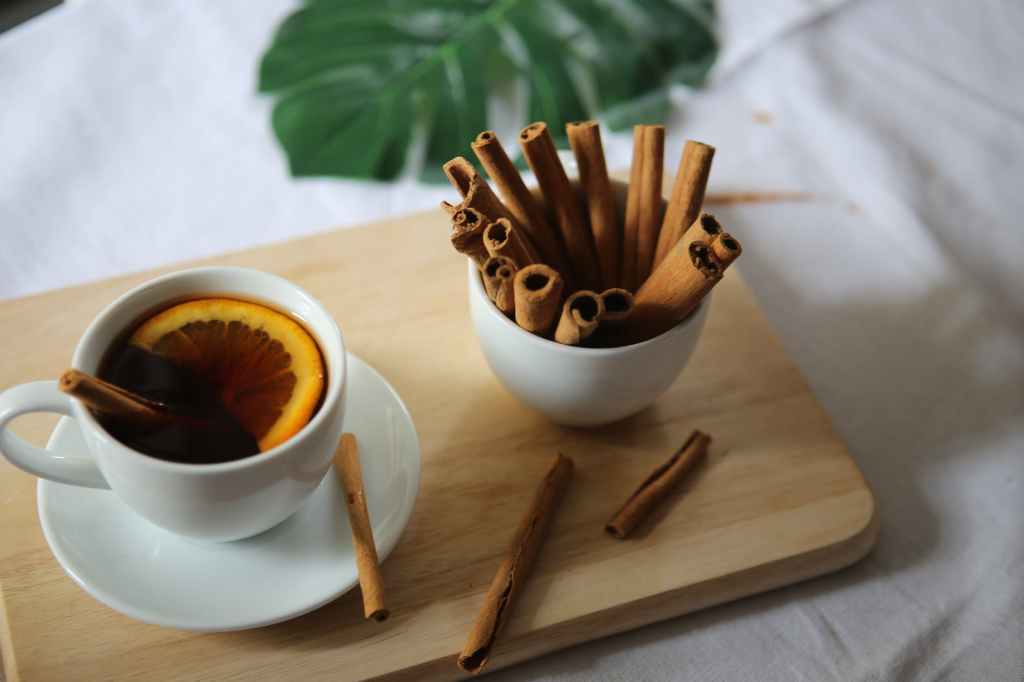 10 awe-inspiring health benefits of cinnamon. Image shows a cup of cinnamon tea and a cup of cinnamon sticks.