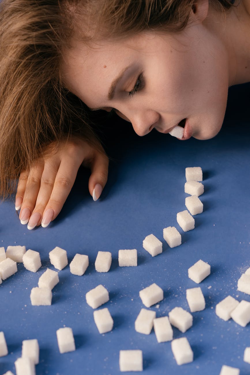 The image shows a woman eating sugar cubes that she has arranged in a pattern. 9 worrying reasons why sugar is bad for your health.