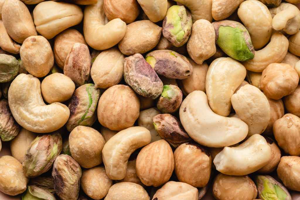 The image shows an assortment of nuts; including pistachios, peanuts, and cashews. 10 Completely Random Facts About Nuts.